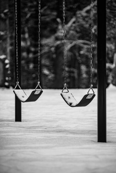 A serene black and white photo of snow-covered swings in a winter playground setting.