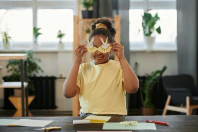 A young girl playfully engages with art indoors, crafting and creativity at its best.