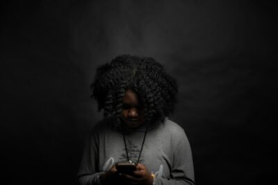 donna in camicia grigia a maniche lunghe che tiene lo smartphone nero